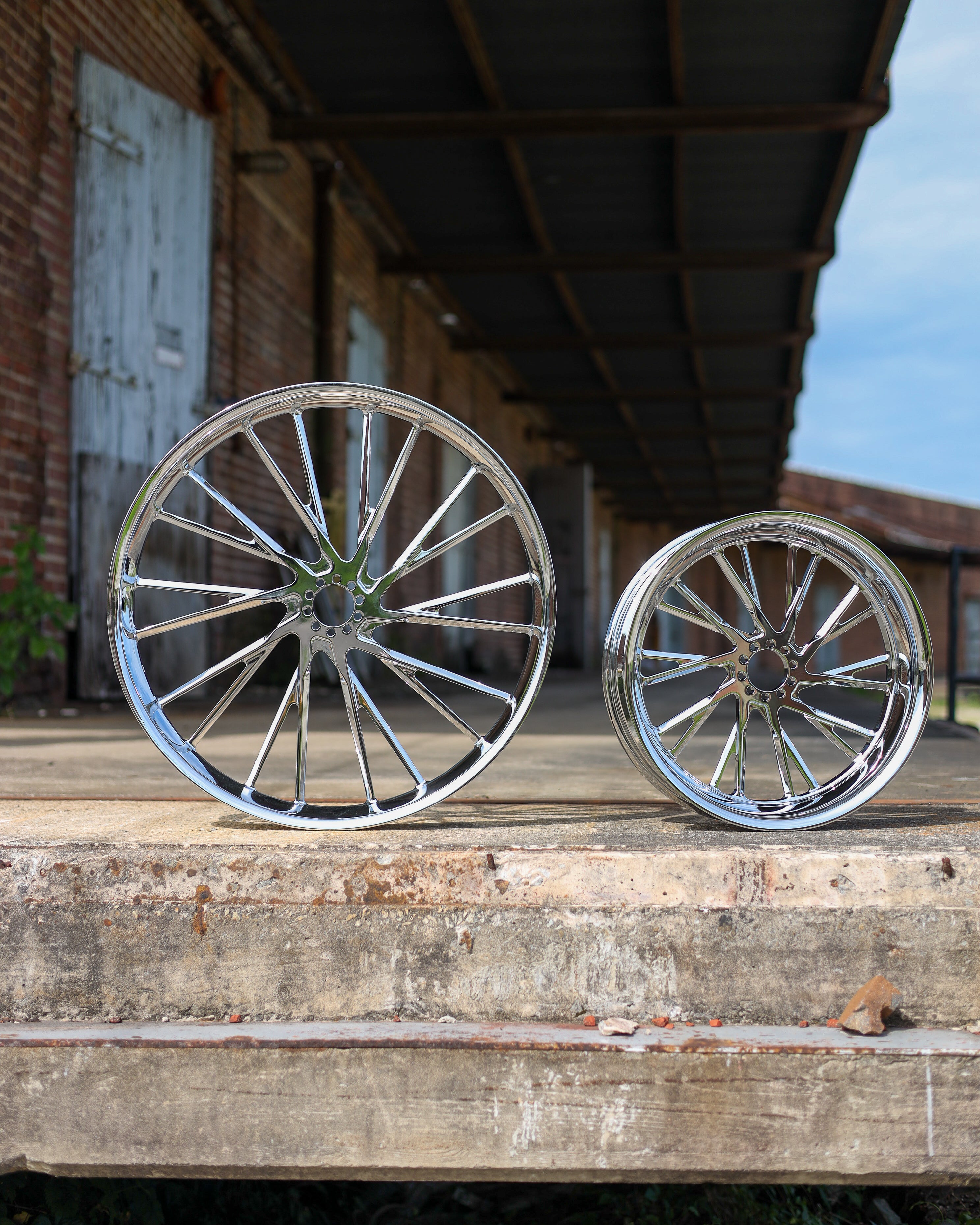 Two chrome wheels on a wooden platform with a rustic background