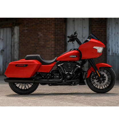 A red and black Harley-Davidson touring motorcycle parked outdoors against a brick wall and weathered metal garage doors.